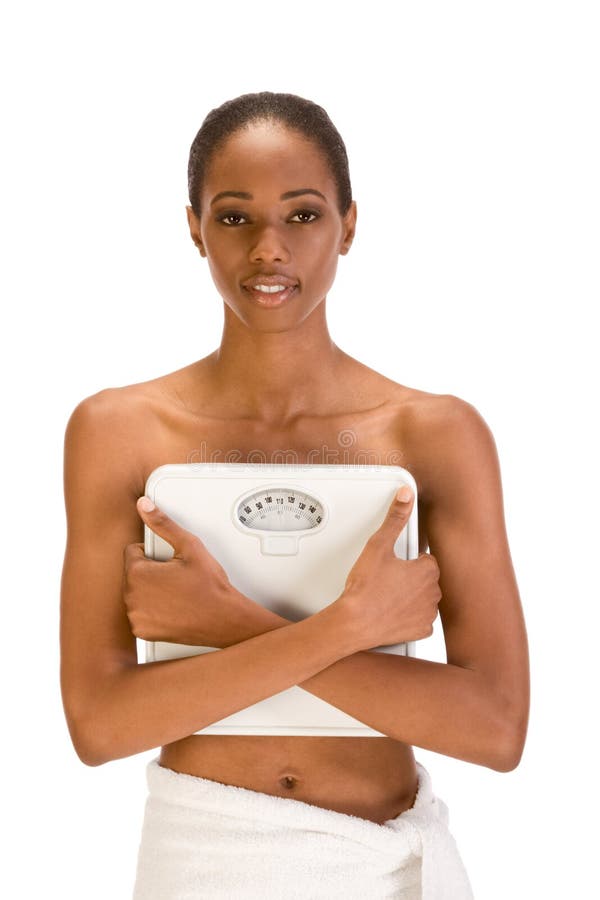 Black woman holding weight scales in front of her. African American topless woman with her hips wrapped in bath towel covers her chest with weighscales confident stock photos