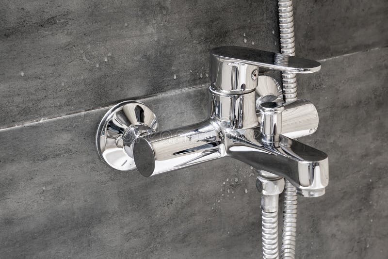 Chrome metal faucet for hot and cold water, with a shower hose, mounted in a wall covered with gray tile imitating concrete royalty free stock photography