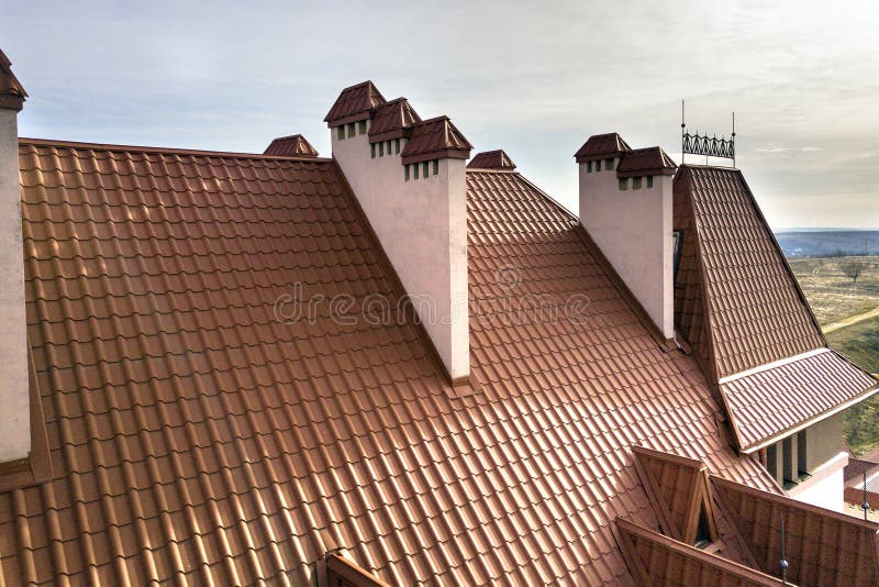 Close-up detail of building steep shingle roof and brick plastered chimneys on house top with metal tile roof. Roofing, repair and royalty free stock image