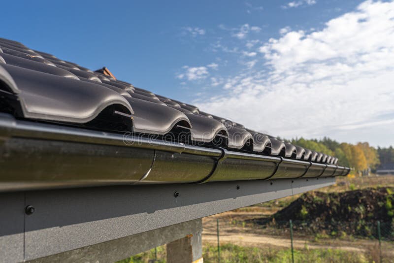 A metal, black gutter on a roof covered with ceramic tiles. Close up shot. stock images