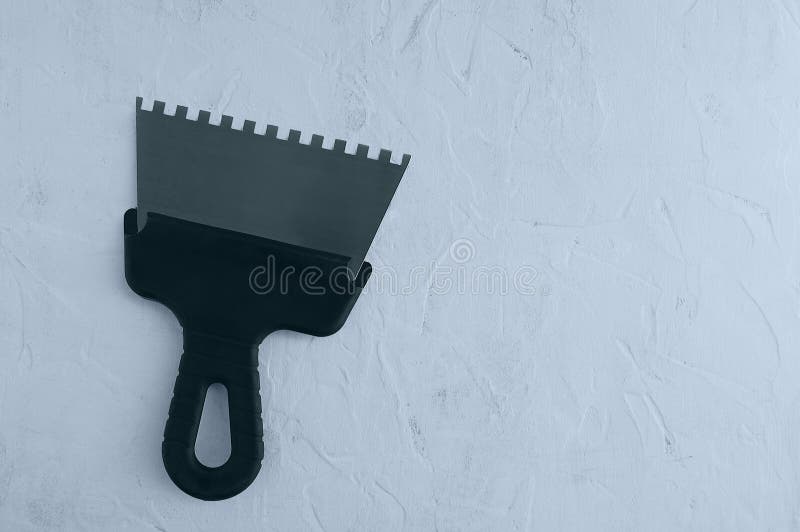 Metal notched construction spatula for tile adhesive with black handle on gray concrete background. View from above stock photography