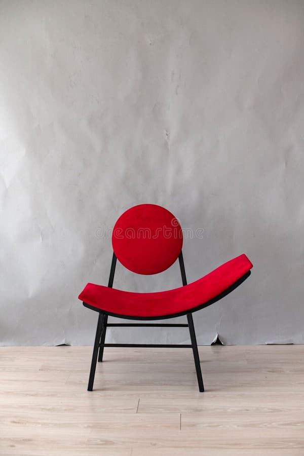 Red stool chair of unusual shape. Minimalistic loft style interior. Red furniture on a background of gray wall. Empty space stock image
