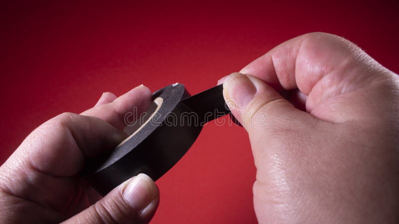 Hand pulling a black insulating tape to show it. This adhesive tape is mainly used to insulate splices of wires and electrical cab stock photo