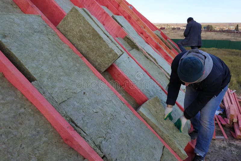The worker puts mineral wool on the roof, insulating the house stock images