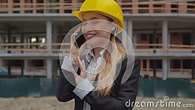 Female architect is excitedly and joyfully talking on the phone against the backdrop of a construction site. Woman in a stock video